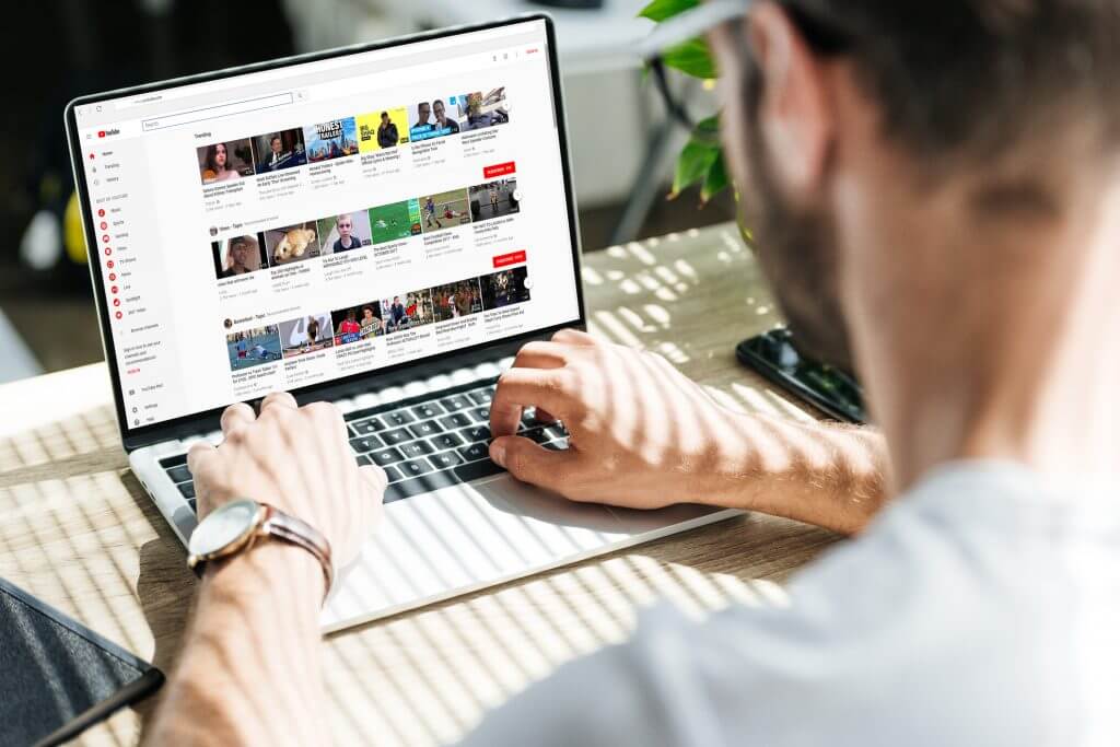 back view of man using laptop with youtube website