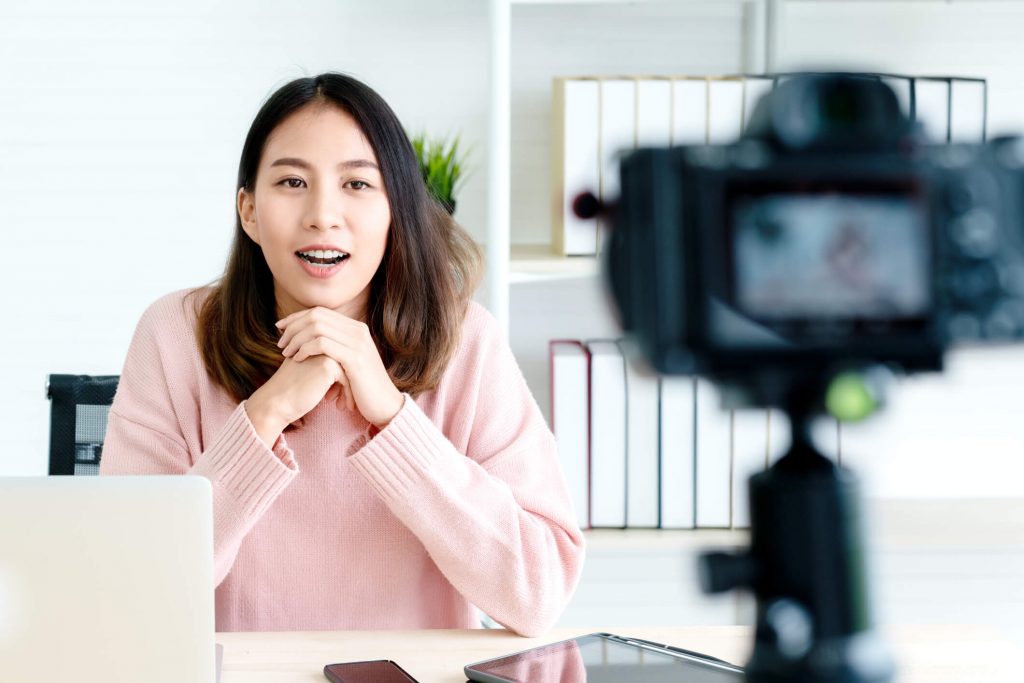 Young woman blogger or vlogger looking at camera and talking on video shooting with technology. Social media