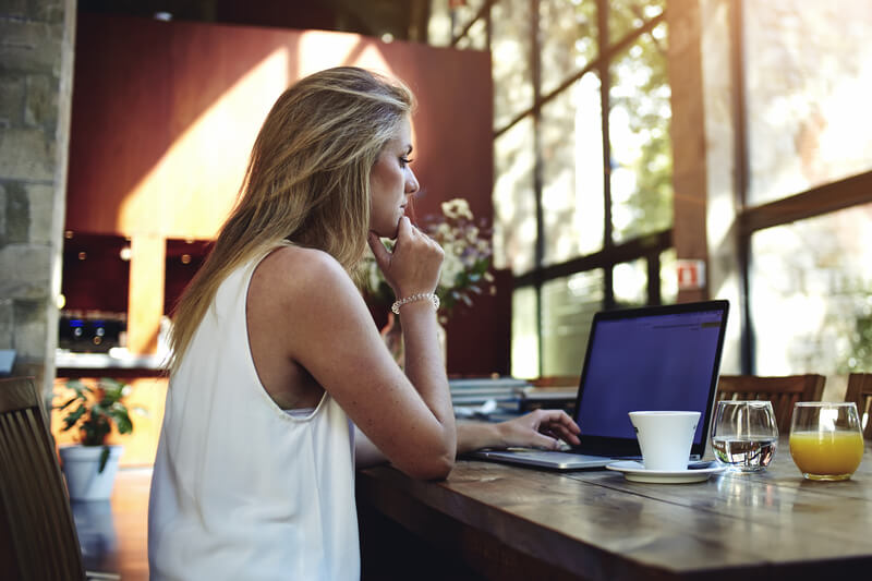 Portrait of a young beautiful woman working on laptop computer while sitting in modern cafe bar interior