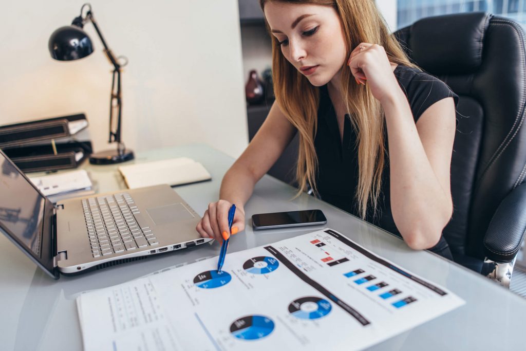 Female businesswoman reading financial report analyzing statistics pointing at pie chart working at her desk