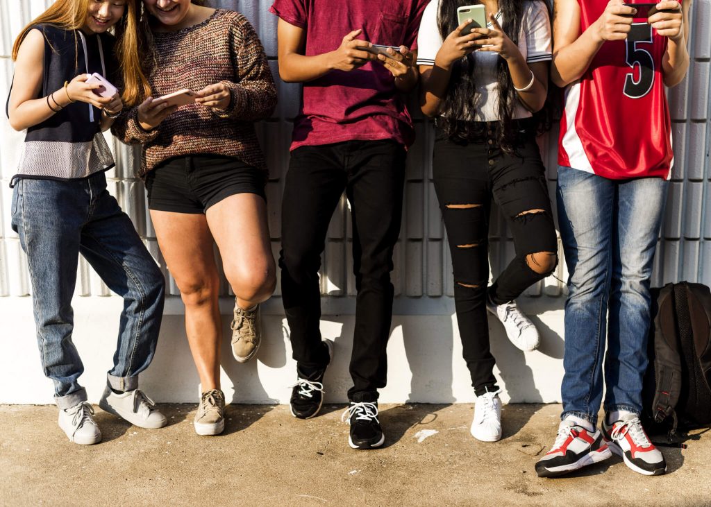 Group of young teenager friends chilling out together using smartphone social media concept