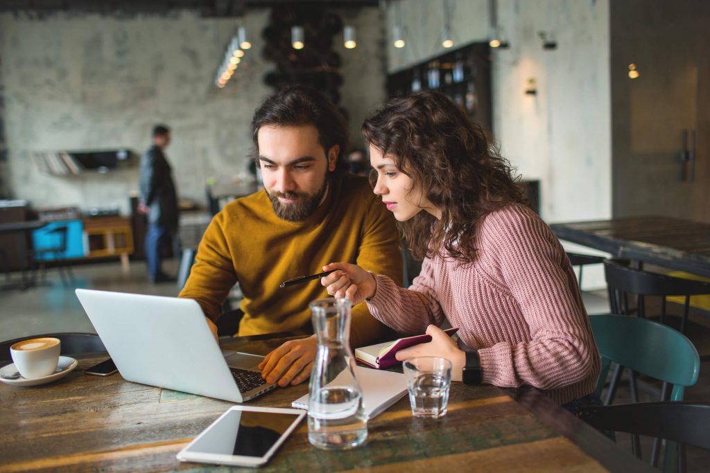 Young hipster male and female working laptop together in cafe